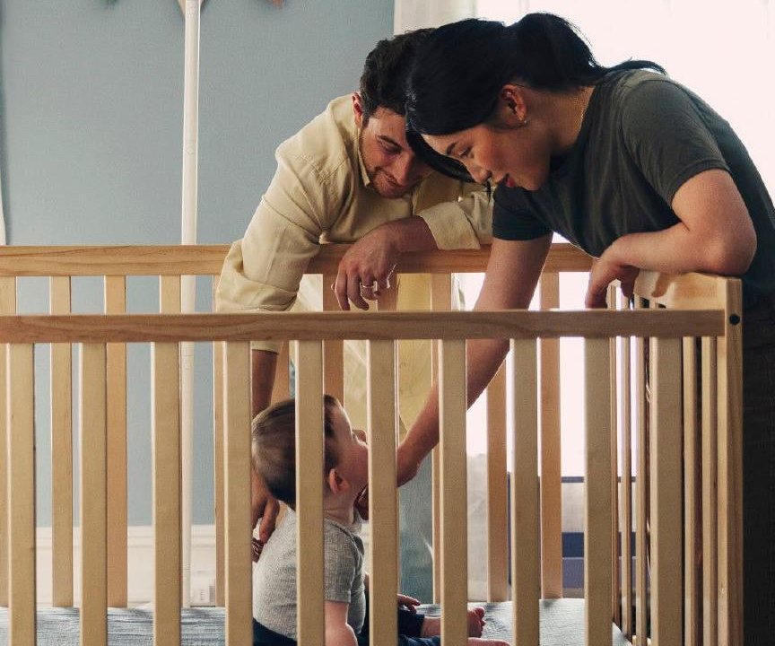 Two parents leaning over a wooden cot, smiling at their baby